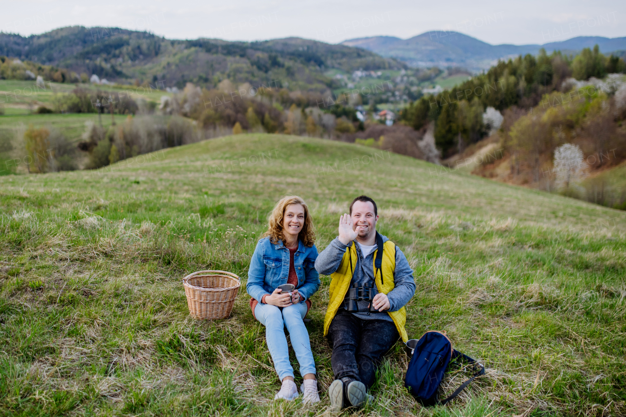 A portrait of happy young man with Down syndrome with his mother resting in nature, sitting and drinking tea.