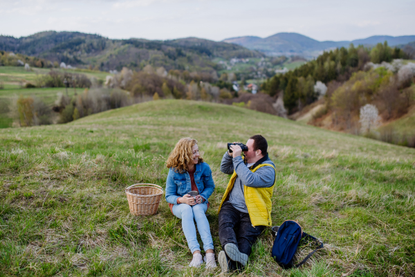 A portrait of happy young man with Down syndrome with his mother resting in nature, sitting and looking at view with binoculars.