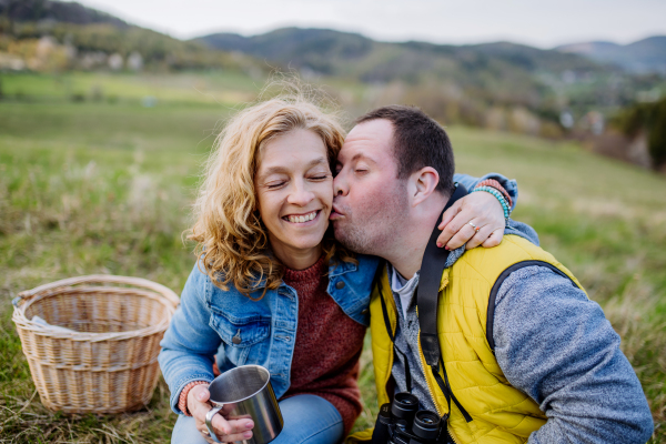 Outdoor portrait of man with down syndrome hugging and kissing his mother, during resting in a green meadow.