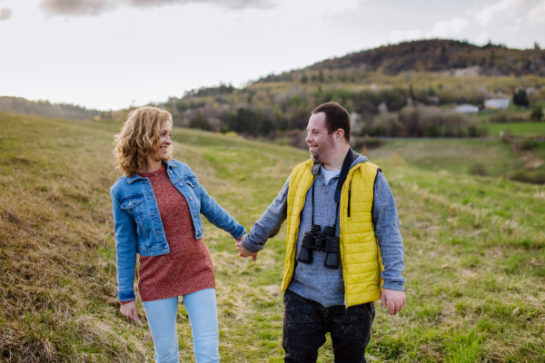 A happy young man with Down syndrome with his mother walking in nature, holding each other hand.