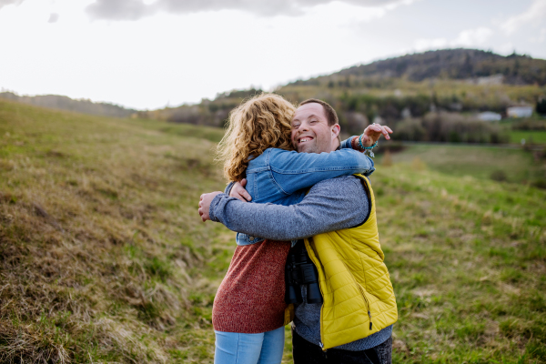 An outdoor portrait of mother hugging her grown up son with Down syndrome, motherhood concept.