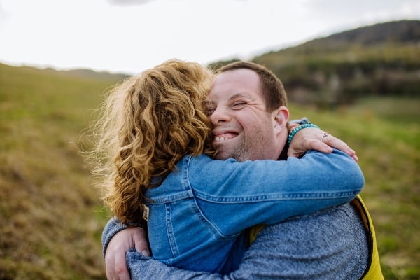 An outdoor portrait of mother hugging her grown up son with Down syndrome, motherhood concept.