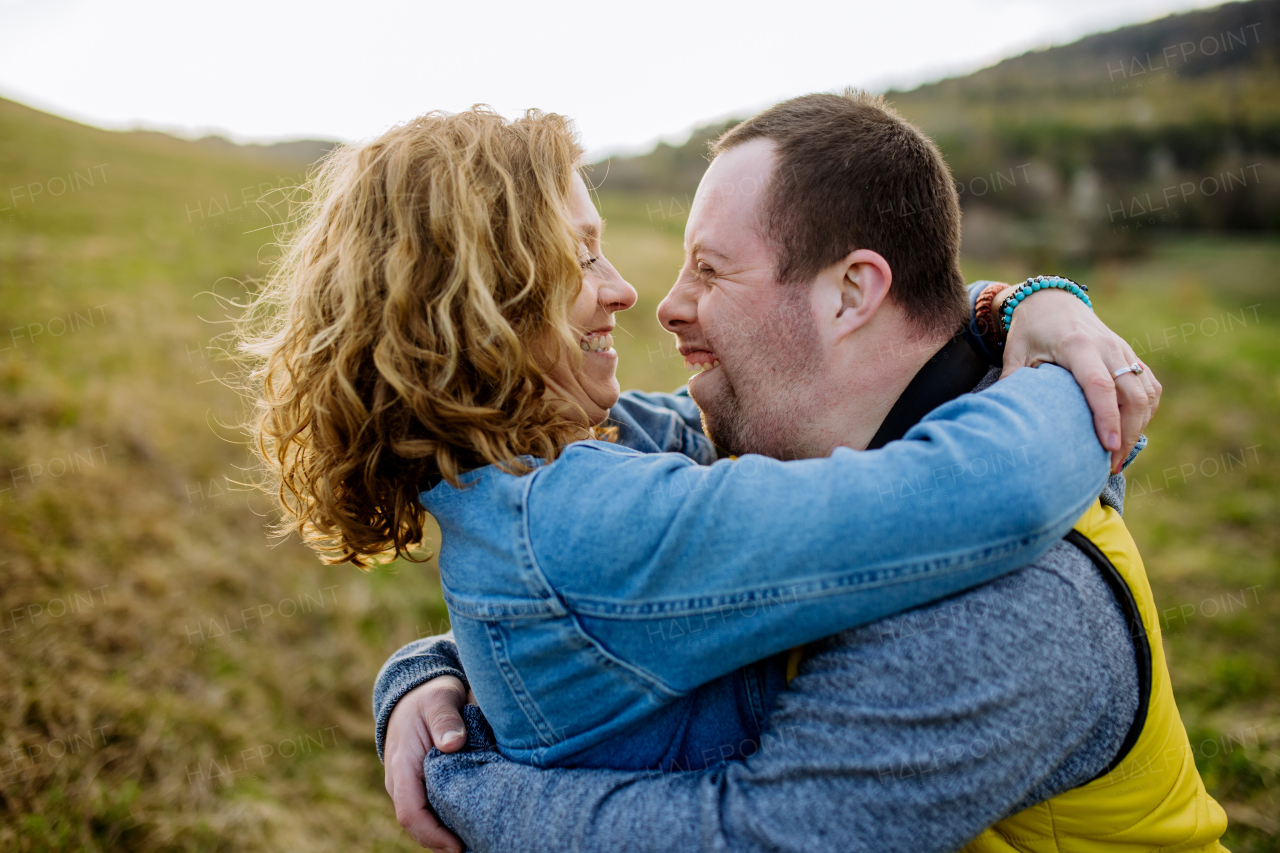 An outdoor portrait of mother hugging her grown up son with Down syndrome, motherhood concept.