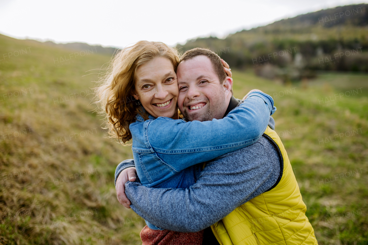 An outdoor portrait of mother hugging her grown up son with Down syndrome, motherhood concept.