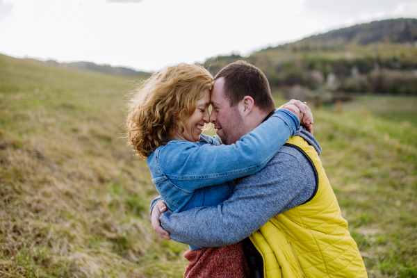 An outdoor portrait of mother hugging her grown up son with Down syndrome, motherhood concept.