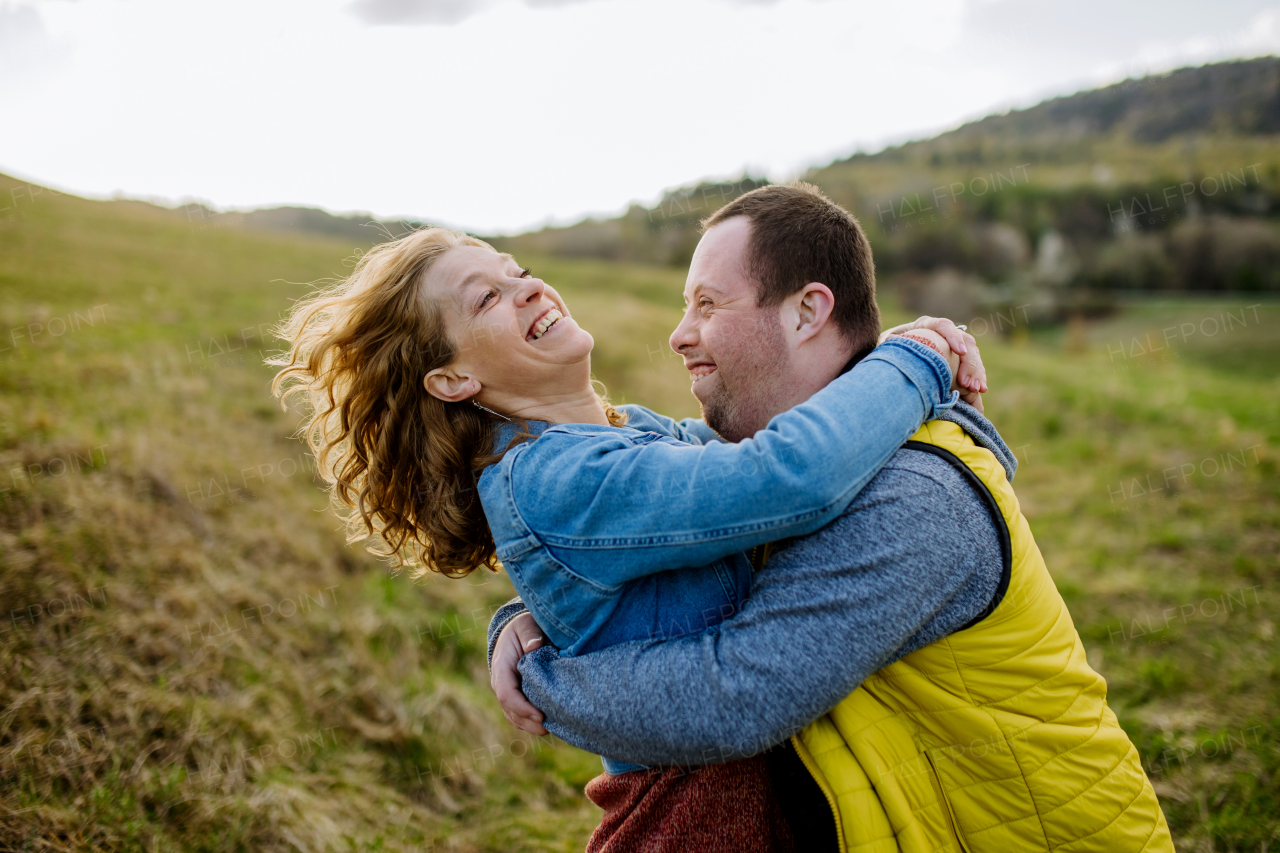 An outdoor portrait of mother hugging her grown up son with Down syndrome, motherhood concept.