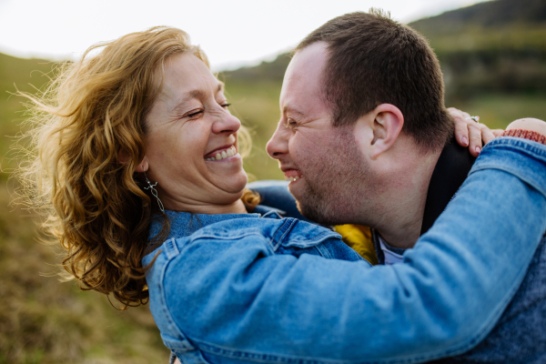 An outdoor portrait of mother hugging her grown up son with Down syndrome, motherhood concept.