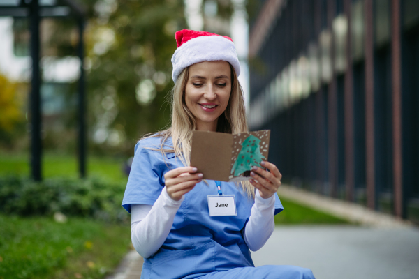 Nurse with christmas hat on head reading christmas card from child patient. Working in hospital on Christmas day. Female doctor working a Christmas shift and can't be with her family.