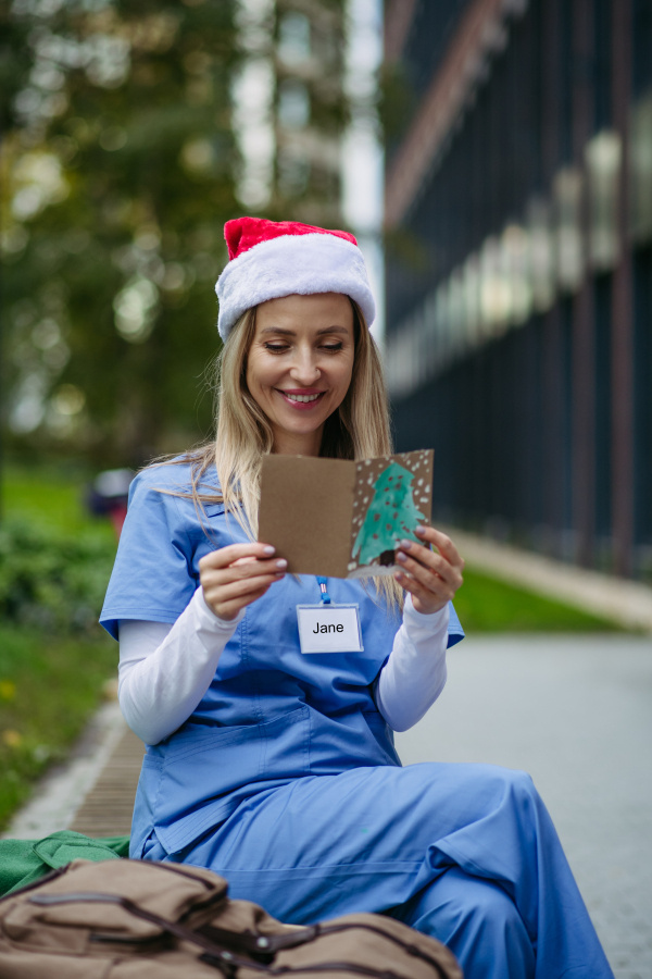 Nurse with christmas hat on head reading christmas card from child patient. Working in hospital on Christmas day. Female doctor working a Christmas shift and can't be with her family.