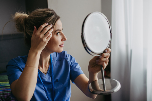 Female nurse or doctor getting ready for work in the morning, brushing hair, making hairstyle in bedroom, dressed in scrubs. Work-life balance for healthcare worker.