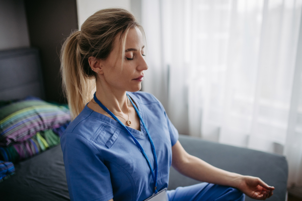 Close up, nurse or doctor enjoying free time at home after work, meditating in bedroom. Work-life balance for a healthcare worker.