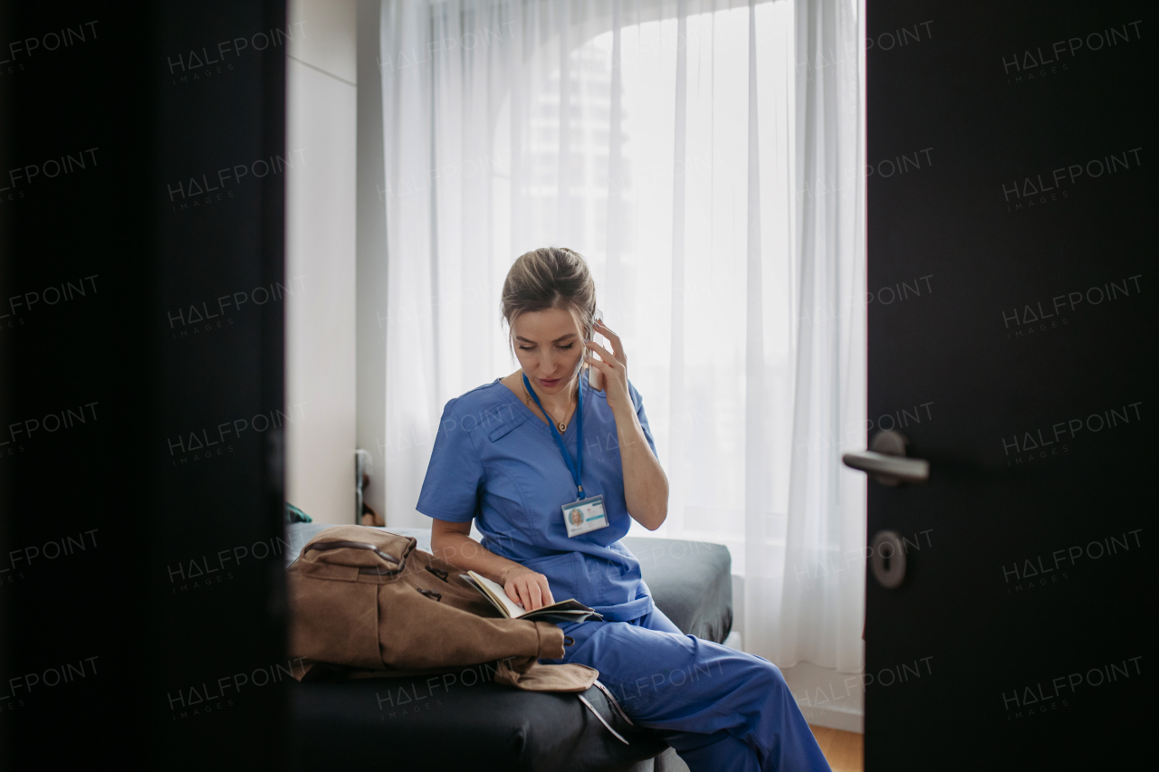 Exhausted doctor in scrubs calling with patient from home, after workday, telemedicine consultation. Work-life balance for healthcare worker.