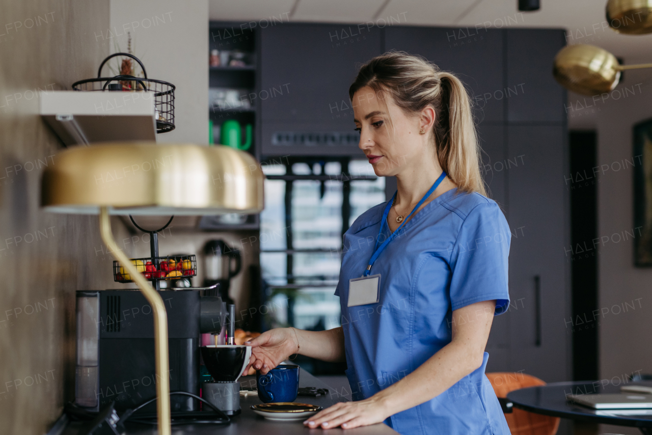 Female nurse or doctor getting ready for work in the morning, making coffee and preparing breakfast, before leaving house, dressed in scrubs. Work-life balance for healthcare worker.