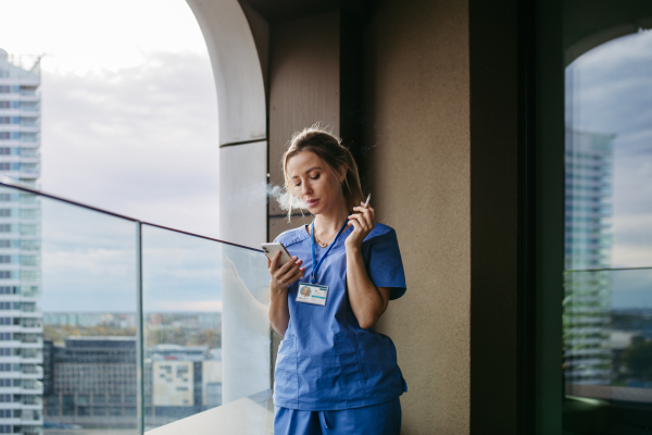 Female nurse smoking cigarette at balcony after work. Doctor feeling overwhelmed and exhausted at work, taking break and smoking.