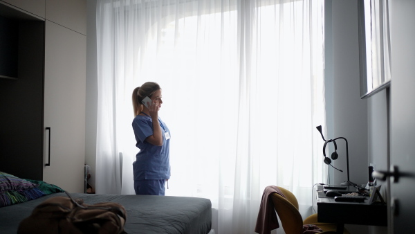 Exhausted doctor in scrubs calling with patient from home, after workday, telemedicine consultation. Work-life balance for healthcare worker.