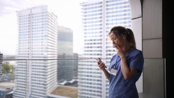 Female nurse smoking cigarette at balcony after work. Doctor feeling overwhelmed and exhausted at work, taking break and smoking.