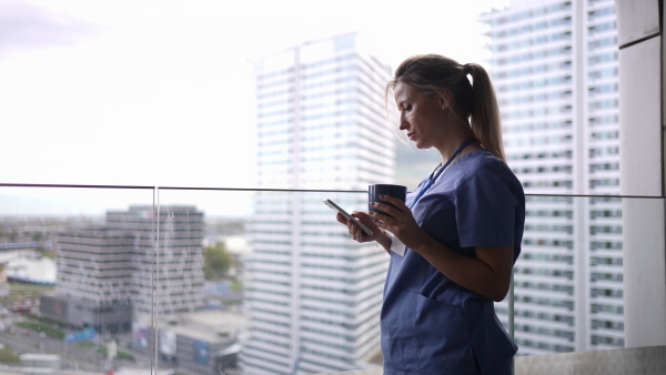 Female nurse smoking cigarette at balcony after work. Doctor feeling overwhelmed and exhausted at work, taking break and smoking.