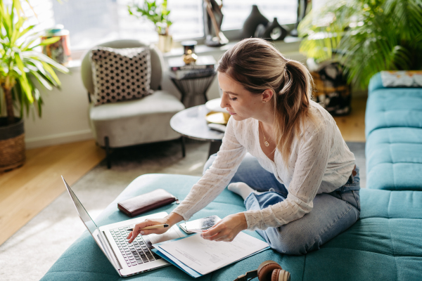 Woman paying bills online, sitting in living room, working on notebook. Online banking, internetbanking at home throught website and app.