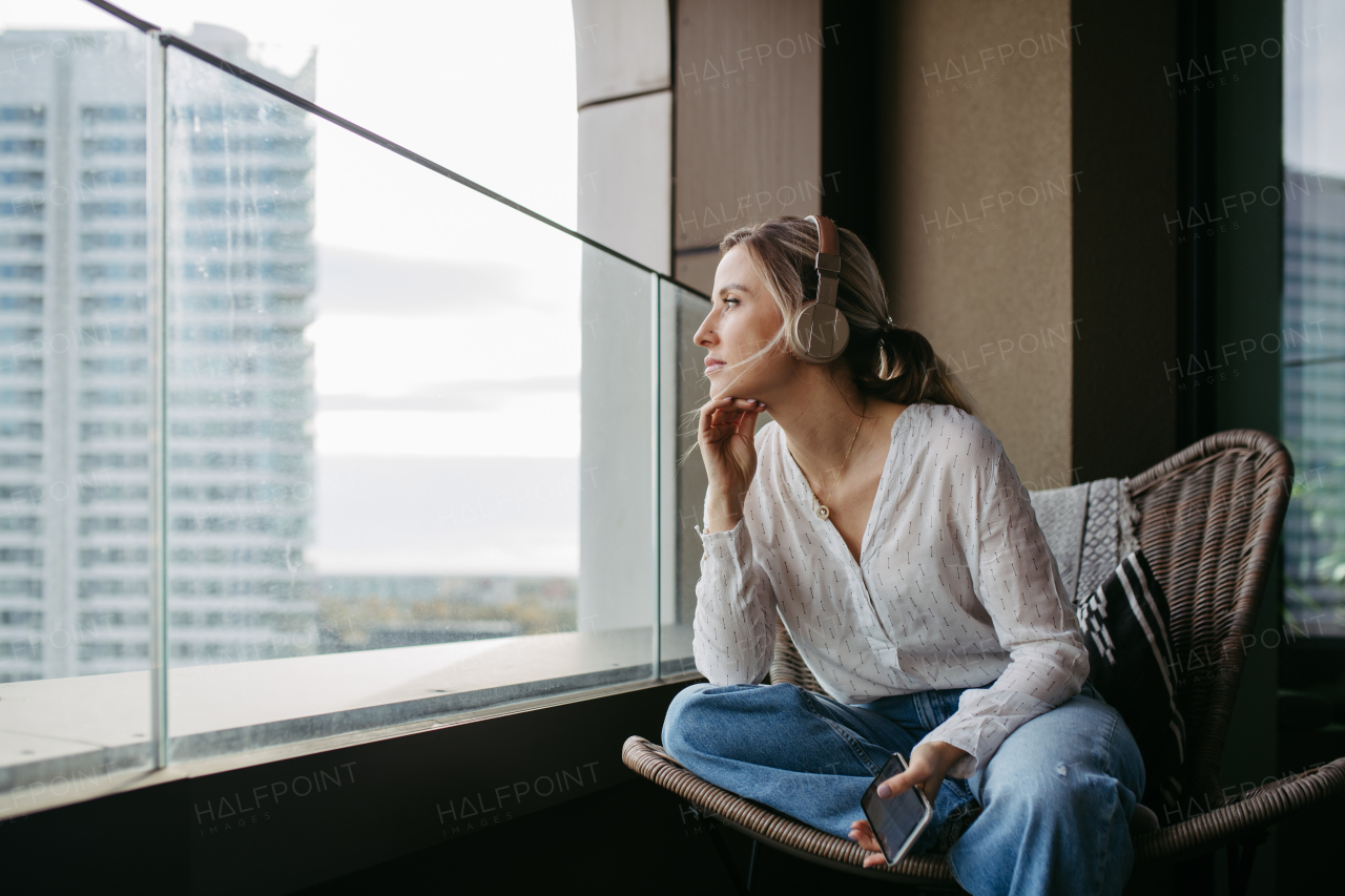 Female nurse or doctor enjoying free time at home after work, sitting by window listening meditation relaxing music. Work-life balance for a healthcare worker.