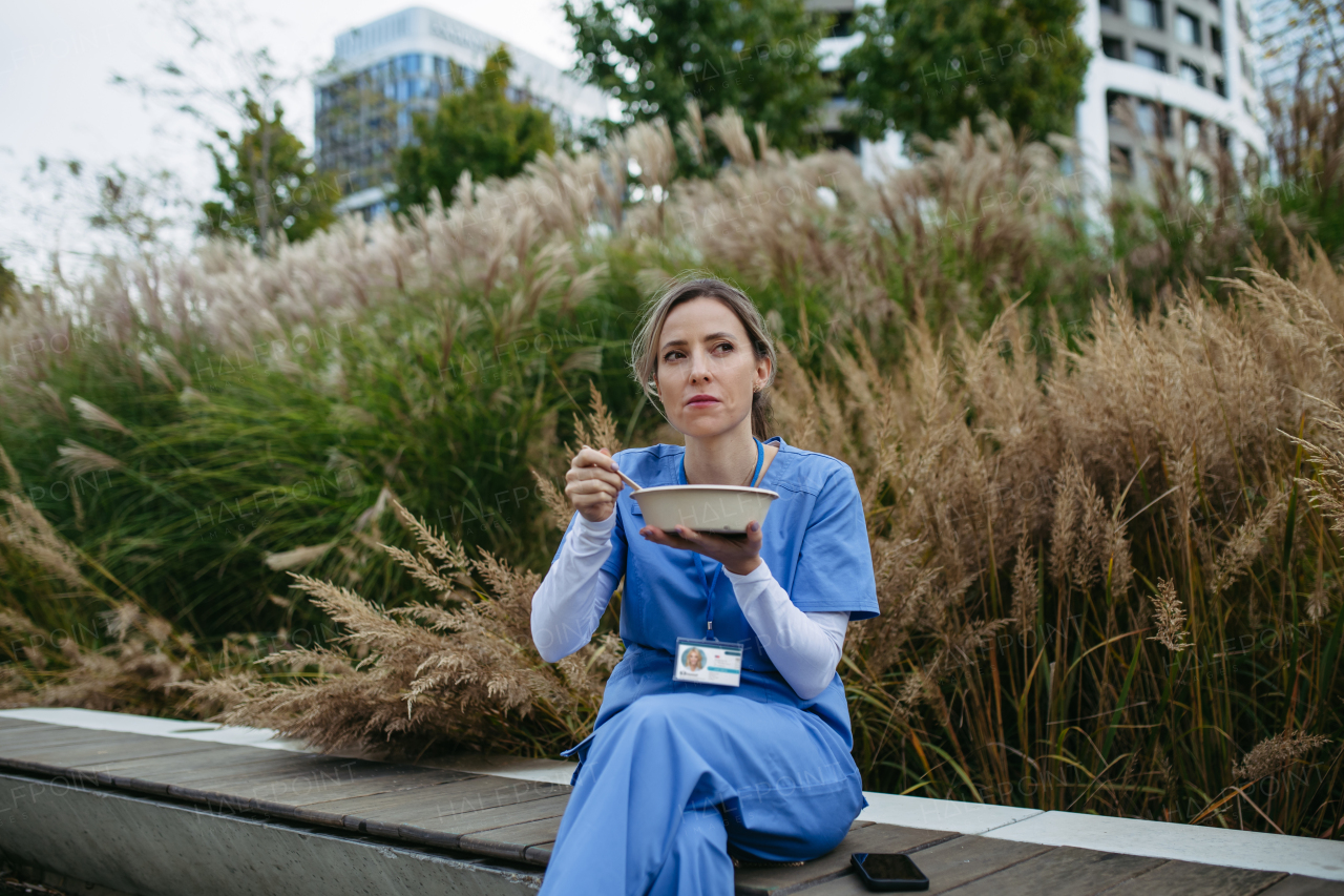 Nurse having healthy lunch or snack in front of hospital building, taking break from work. Importance of breaks in healthcare.