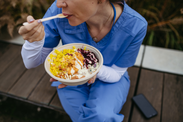 Nurse having healthy balanced lunch in front of hospital building, taking break from work. Importance of breaks in healthcare.