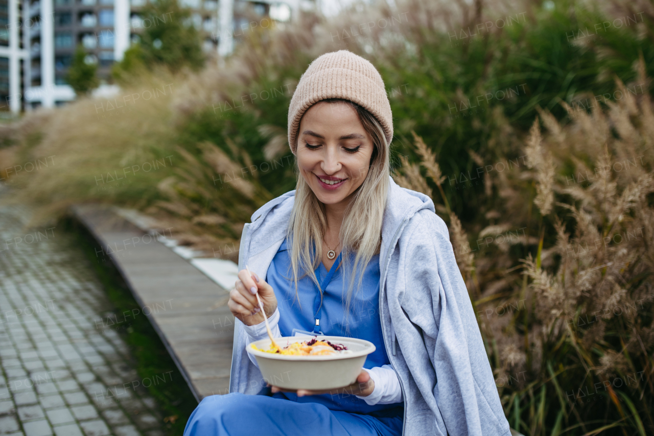 Nurse having healthy lunch or snack in front of hospital building, taking break from work. Importance of breaks in healthcare.