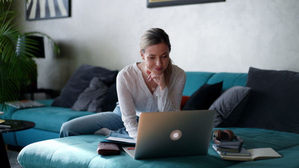 Woman paying bills online, sitting in living room, working on notebook. Online banking, internetbanking at home throught website and app.