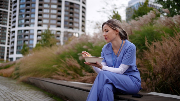 Nurse having healthy lunch or snack in front of hospital building, taking break from work. Importance of breaks in healthcare.