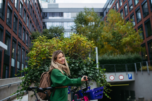 Beautiful nurse using public bike sharing system, renting city bicycle. Doctor in city leaving hospital by bike after long workday.