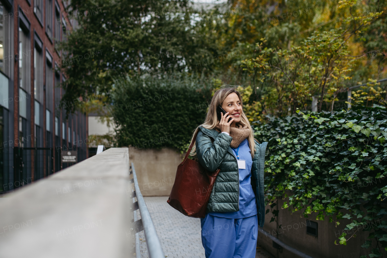 Female nurse or doctor going home from work, phone calling on smartphone. Work-life balance of healthcare worker as parent and partner.