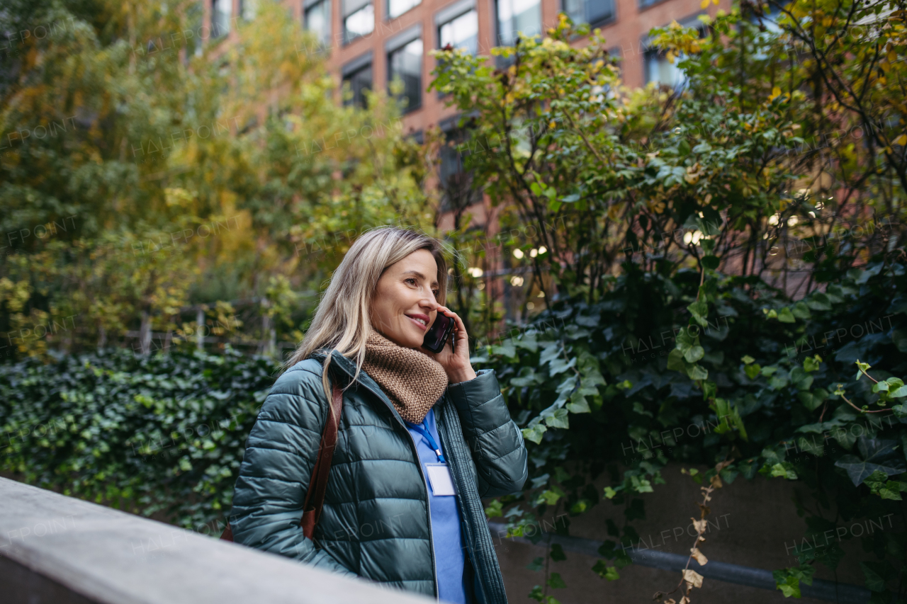 Female nurse or doctor going home from work, phone calling on smartphone. Work-life balance of healthcare worker.