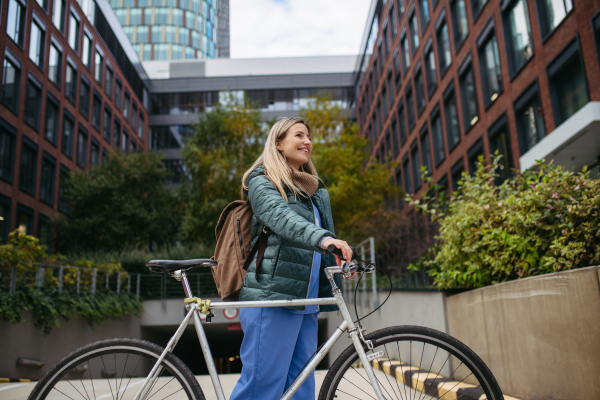 Beautiful nurse commuting through the city by bike. Doctor city leaving the hospital by bike after long workday. Low angle shot.