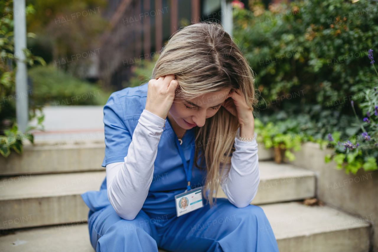 Young female doctor feeling overwhelmed at work, sitting on stairs. Healthcare workers having stressful job, feeling exhausted. Burnout syndrome for doctors and nurses.