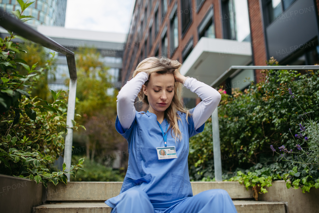 Young female doctor feeling overwhelmed at work, sitting on stairs. Healthcare workers having stressful job, feeling exhausted. Burnout syndrome for doctors and nurses.