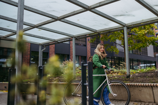 Beautiful nurse commuting through the city by bike. Doctor city leaving the hospital by bike after long workday. Low angle shot.