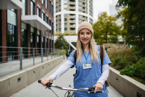 Beautiful nurse commuting through the city by bike. Doctor city commuter traveling from work by bike after long workday in clinic.