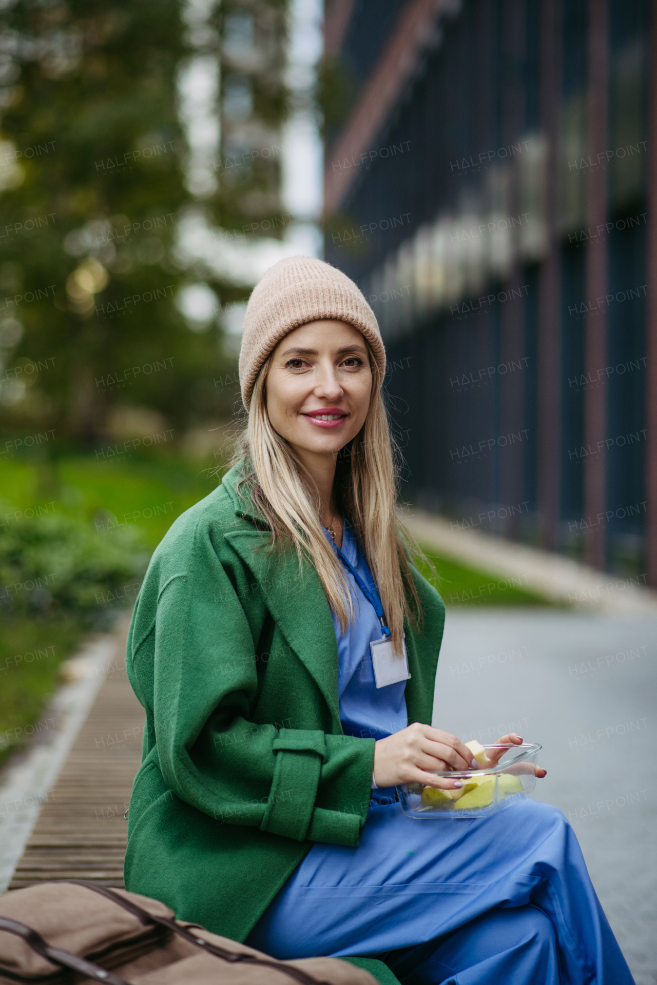 Nurse having healthy fruit snack in front of hospital building, taking break from work. Importance of breaks in healthcare.