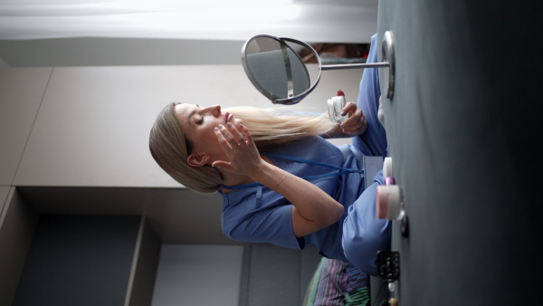 Female nurse or doctor getting ready for work in the morning, doing makeup, skincare in bedroom, dressed in scrubs. Work-life balance for healthcare worker.