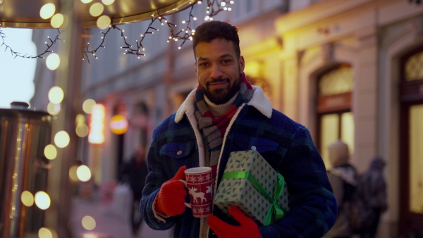 Happy smiling multiracial man with presents at Christmas market, buying a punch.