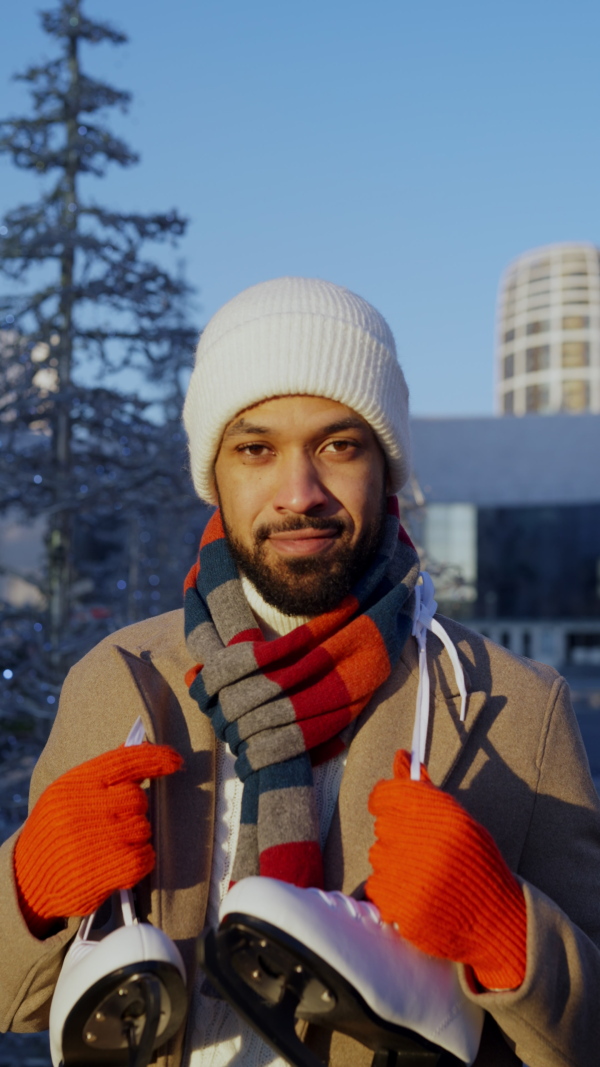 Young multiracial man with ice skates, outdoor in public ice rink. Vertical view.