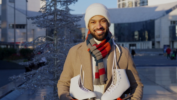 Young multiracial man with ice skates, outdoor in public ice rink.