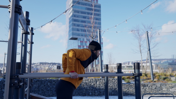 Young man doing exercise in outdoor gym, during winter.