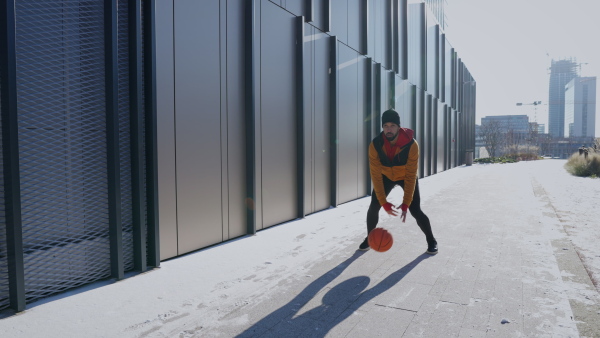 Young man playing basketball in city during winter season.