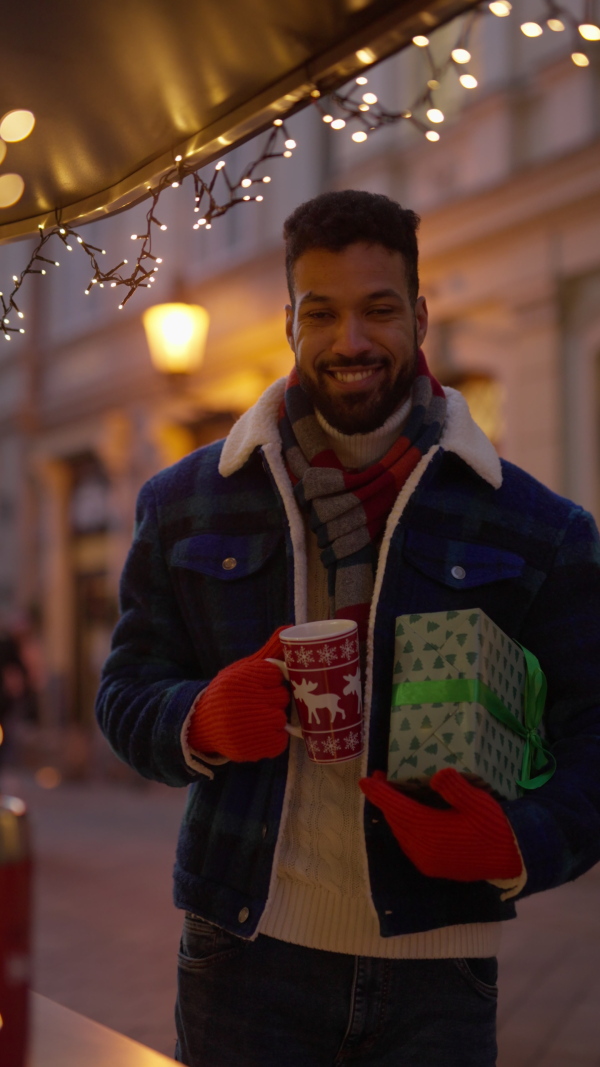 Happy smiling multiracial man with presents at Christmas market. Vertical view.