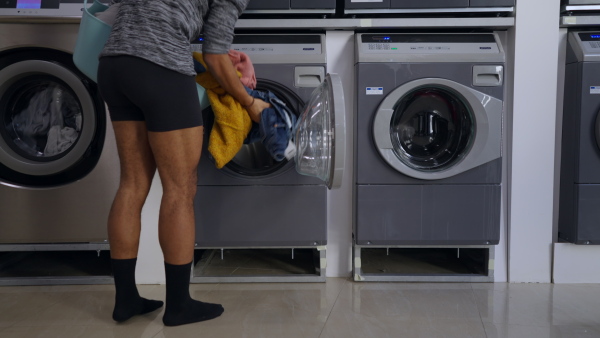 Young half-naked multiracial man in laundry, loading washing machine.