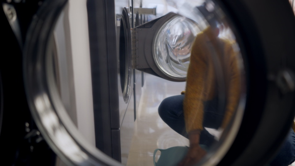 Young multiracial man in laundry, loading washing machine.