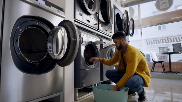 Young multiracial man in laundry, loading washing machine.