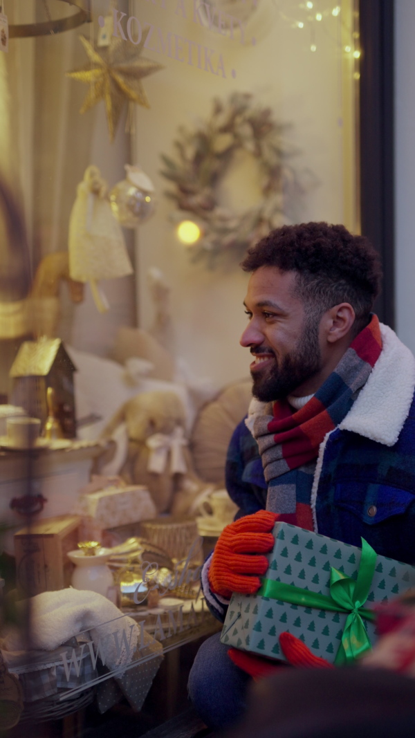 Happy smiling multiracial man with presents at Christmas market. Vertical view.