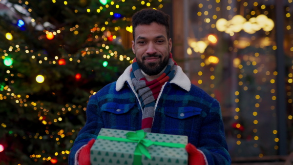 Happy smiling multiracial man with presents at Christmas market.