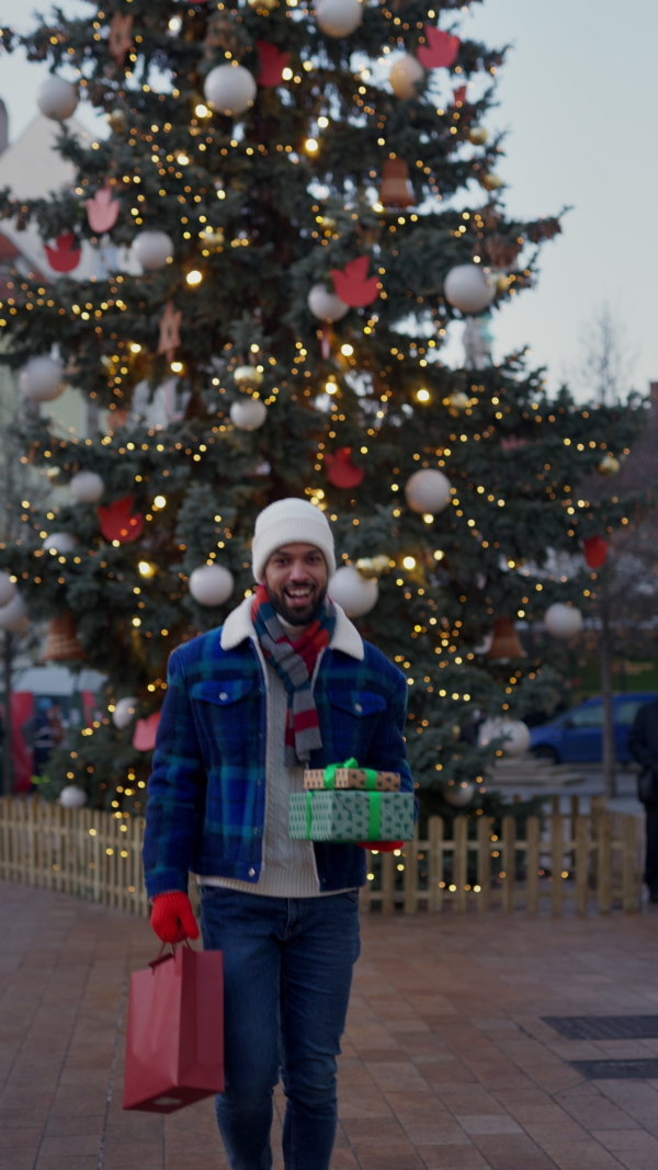 Happy smiling multiracial man with presents at Christmas market. Vertical view.